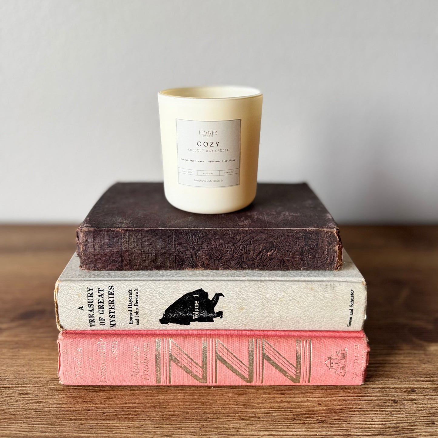 Stack of books with a candle labeled 'cozy' on a wooden surface