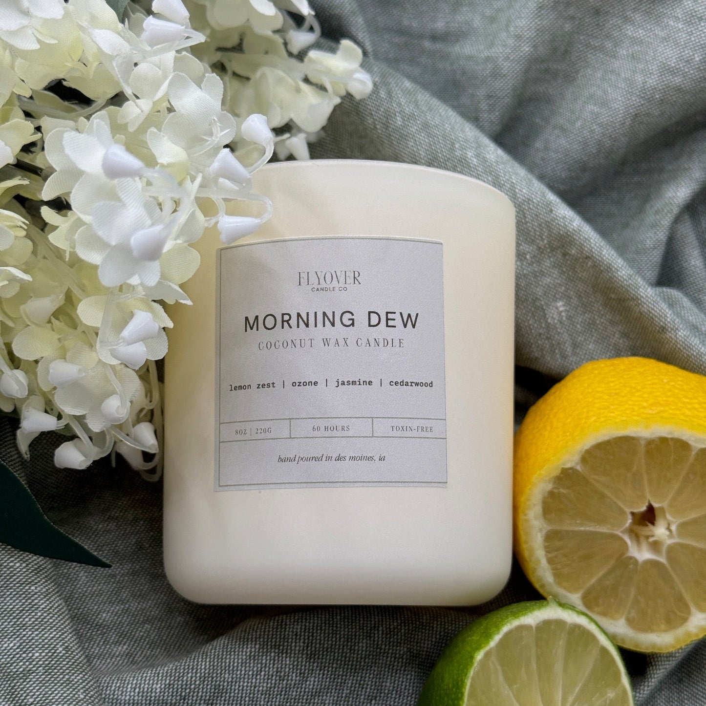 Candle labeled 'Morning Dew' with lemons and flowers on a gray fabric background