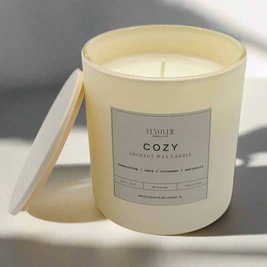 Cream-colored candle in a glass jar with a label on a white background