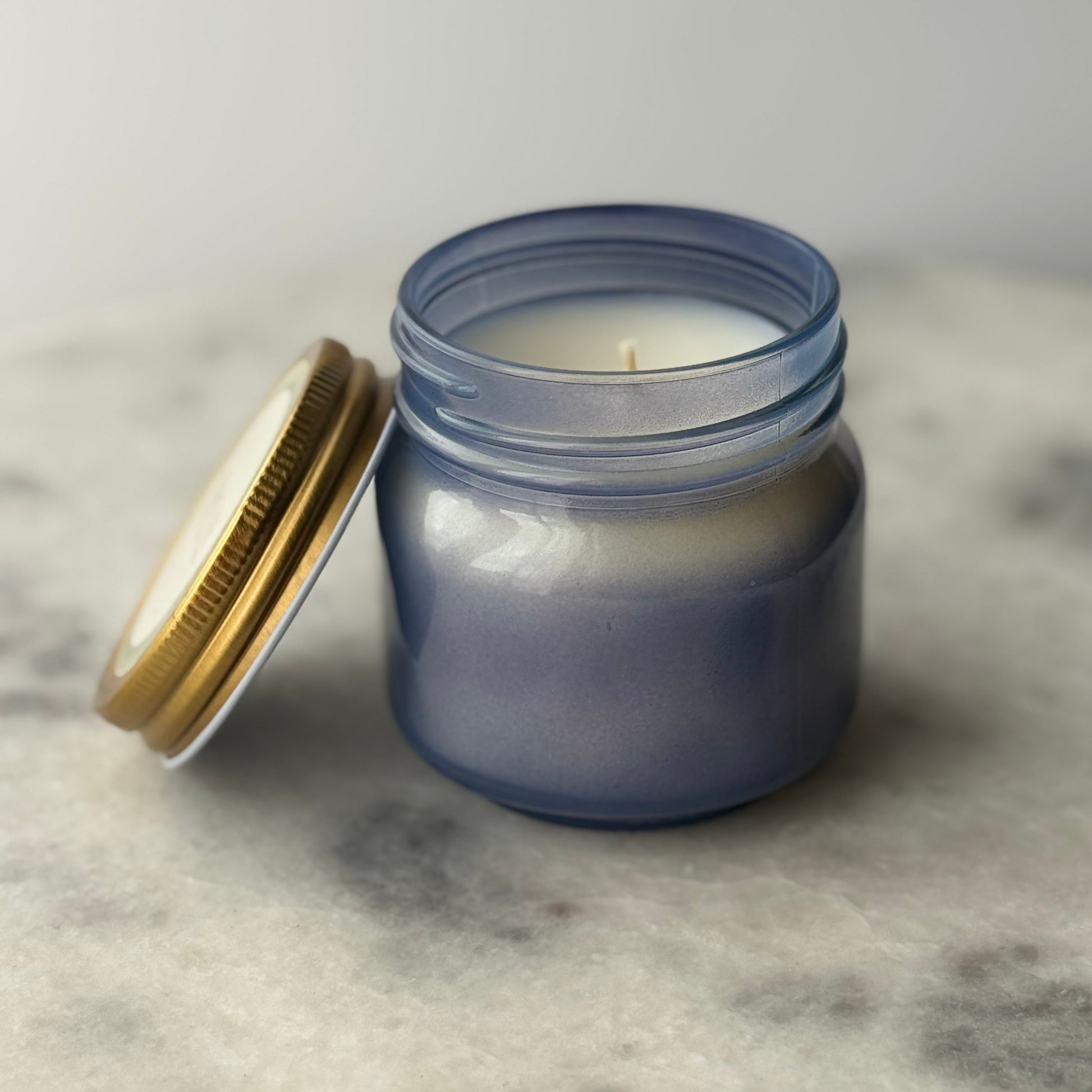 Blue candle in a glass jar with a gold lid on a marble surface