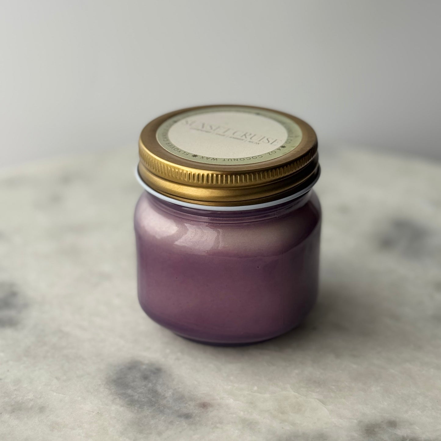 Purple candle in a glass jar with a gold lid on a marble surface