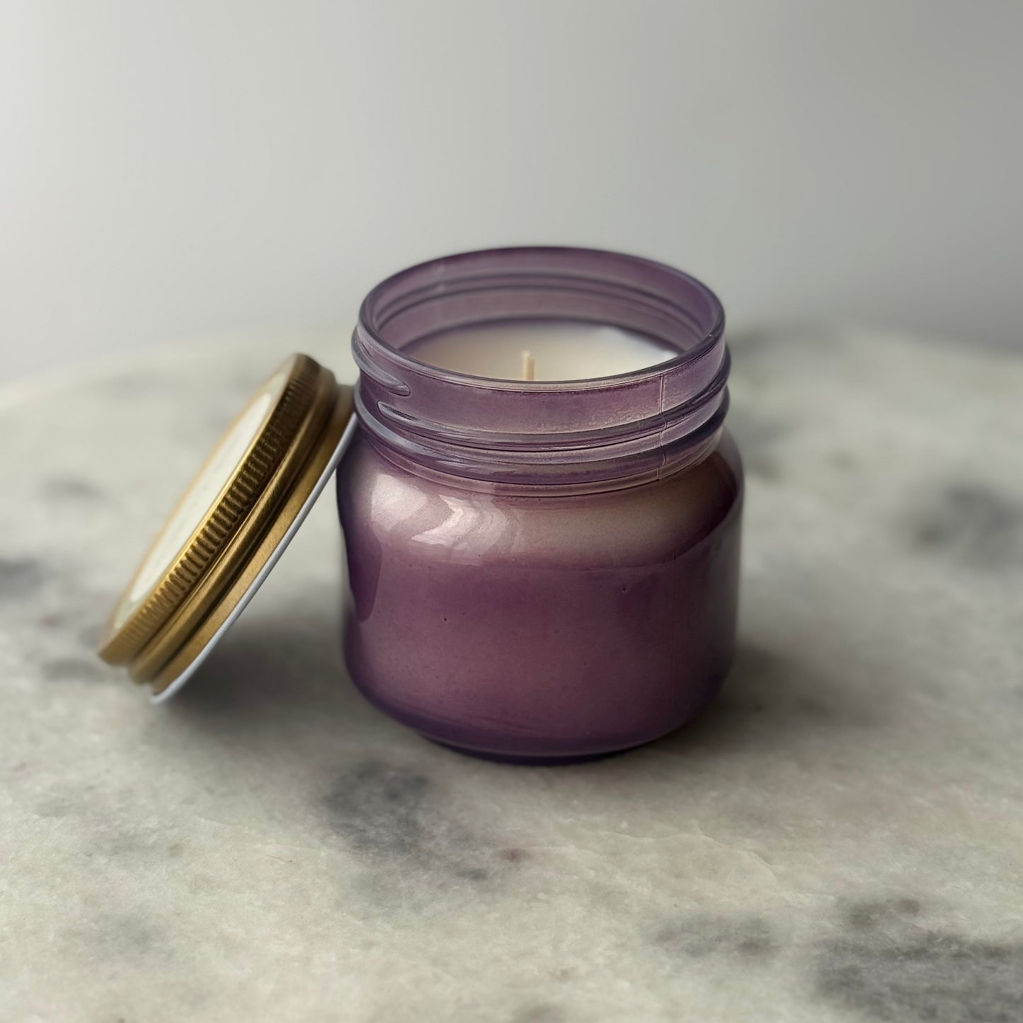 Purple candle in a glass jar with a gold lid on a marble surface