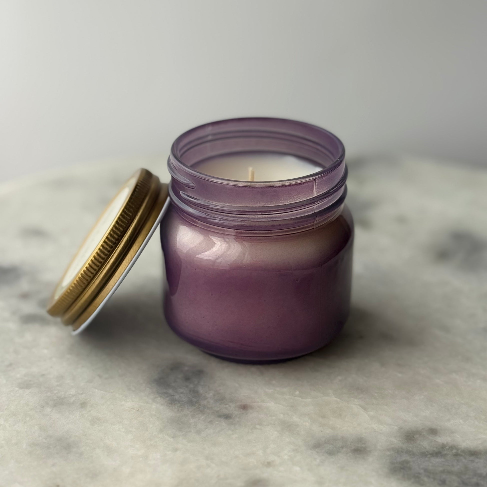 Purple candle in a glass jar with a gold lid on a marble surface