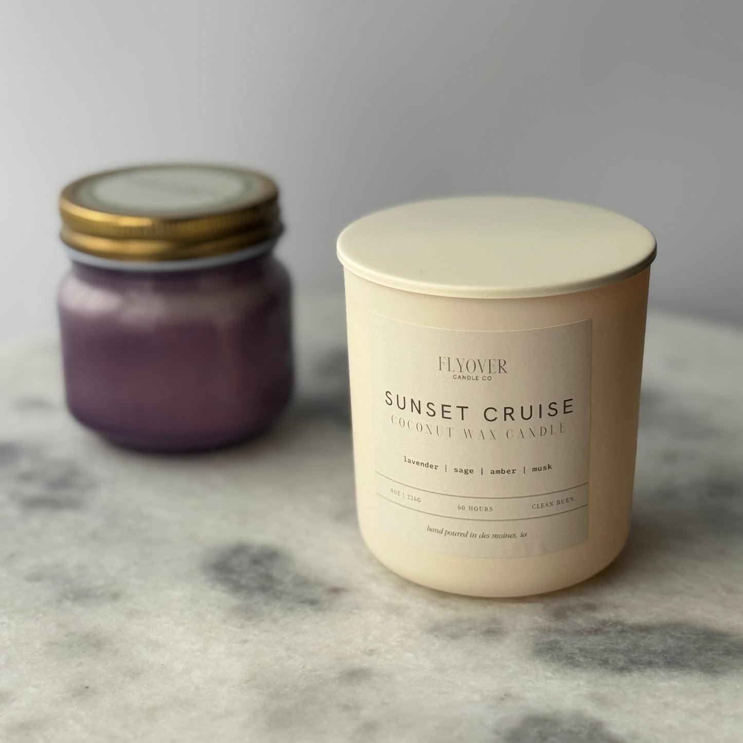 Two candles, one purple and one ivory, on a marble surface.