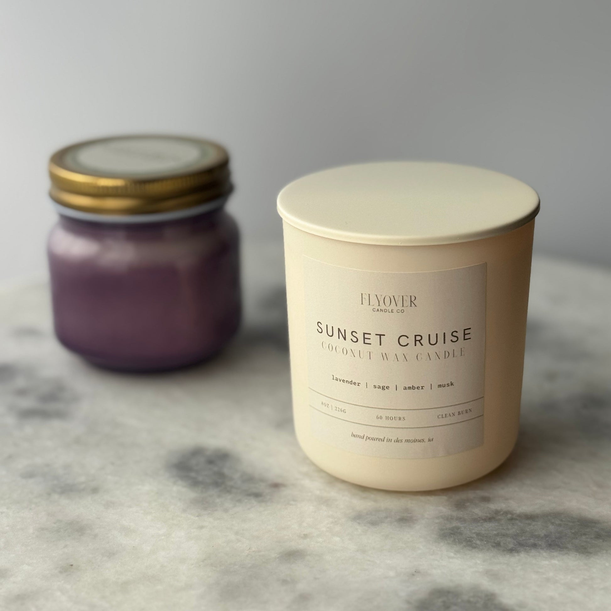 Two candles, one purple and one ivory, on a marble surface.