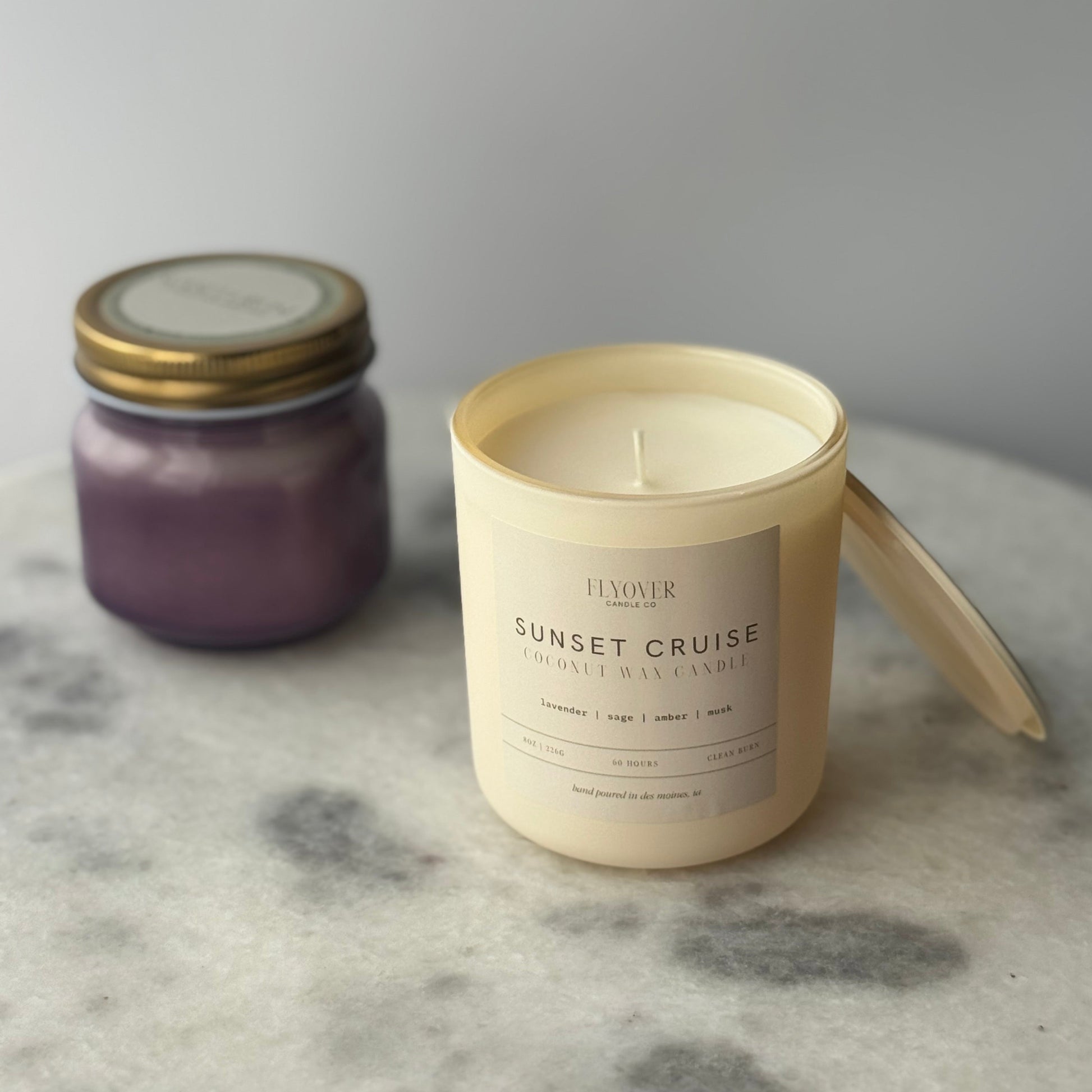 Two candles, one purple and one labeled 'Sunset Cruise', on a marble surface.