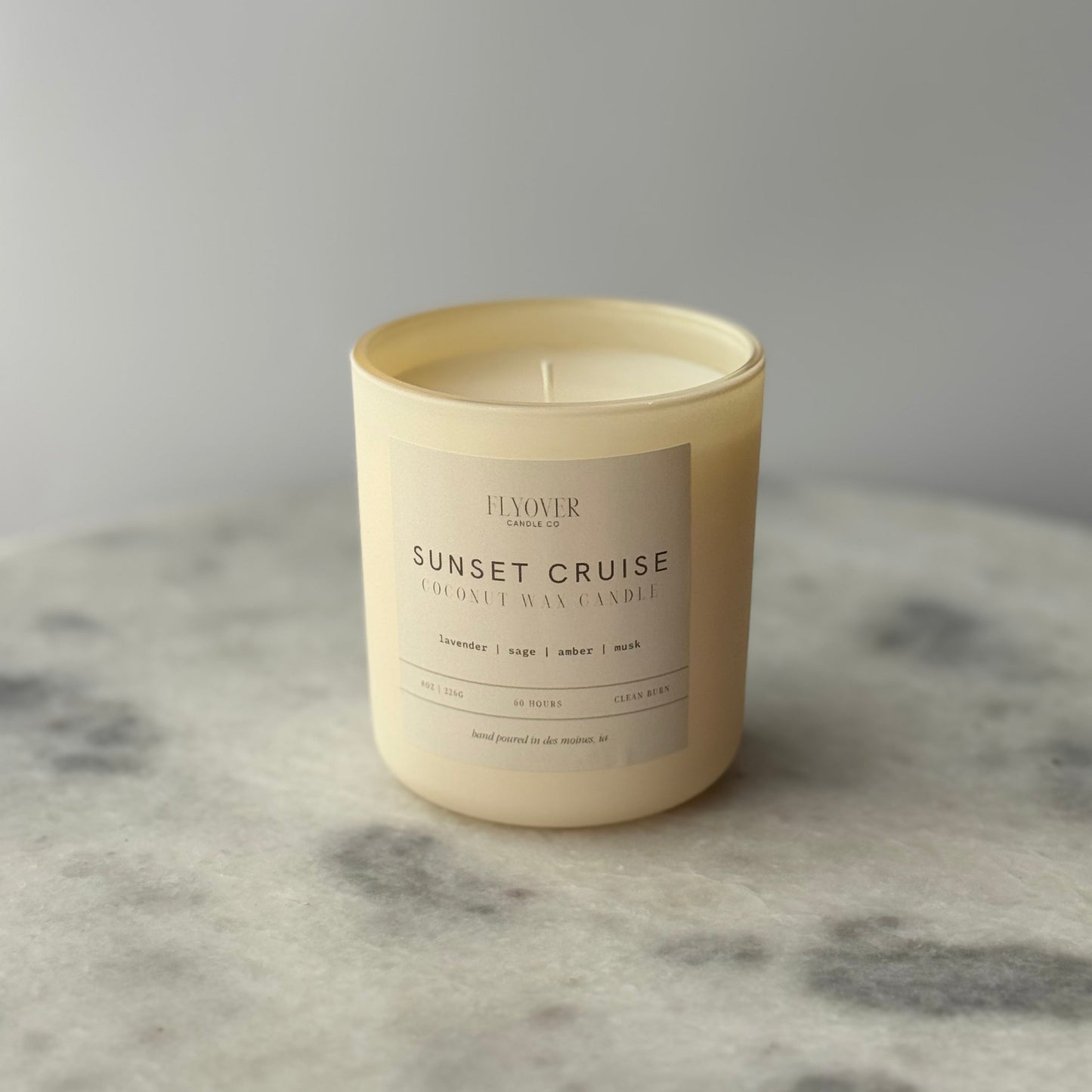 Candle labeled 'Sunset Cruise' on a marble surface with a gray background