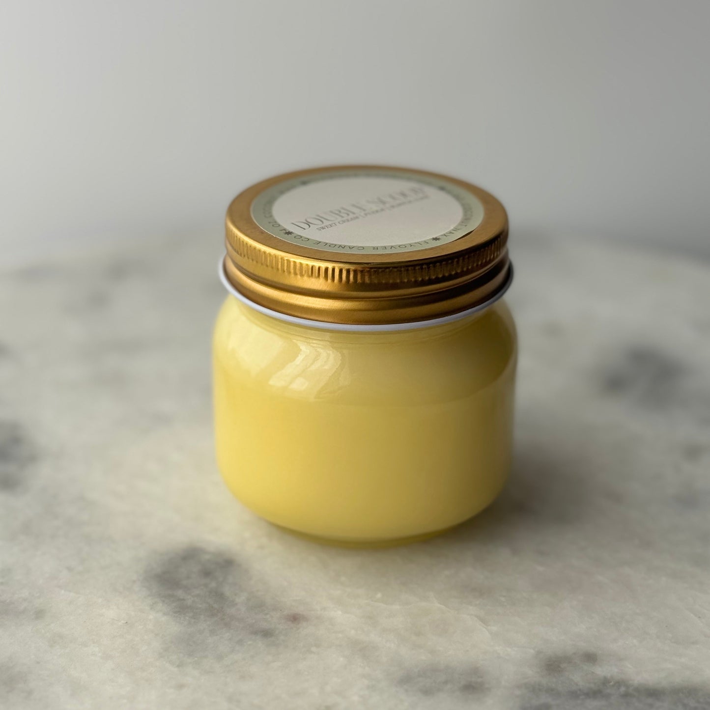 yellow mason jar candle with a gold lid on a marble surface