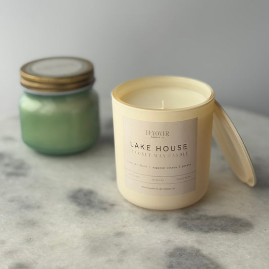 Two candles, one green and one beige with 'Lake House' label, on a marble surface.