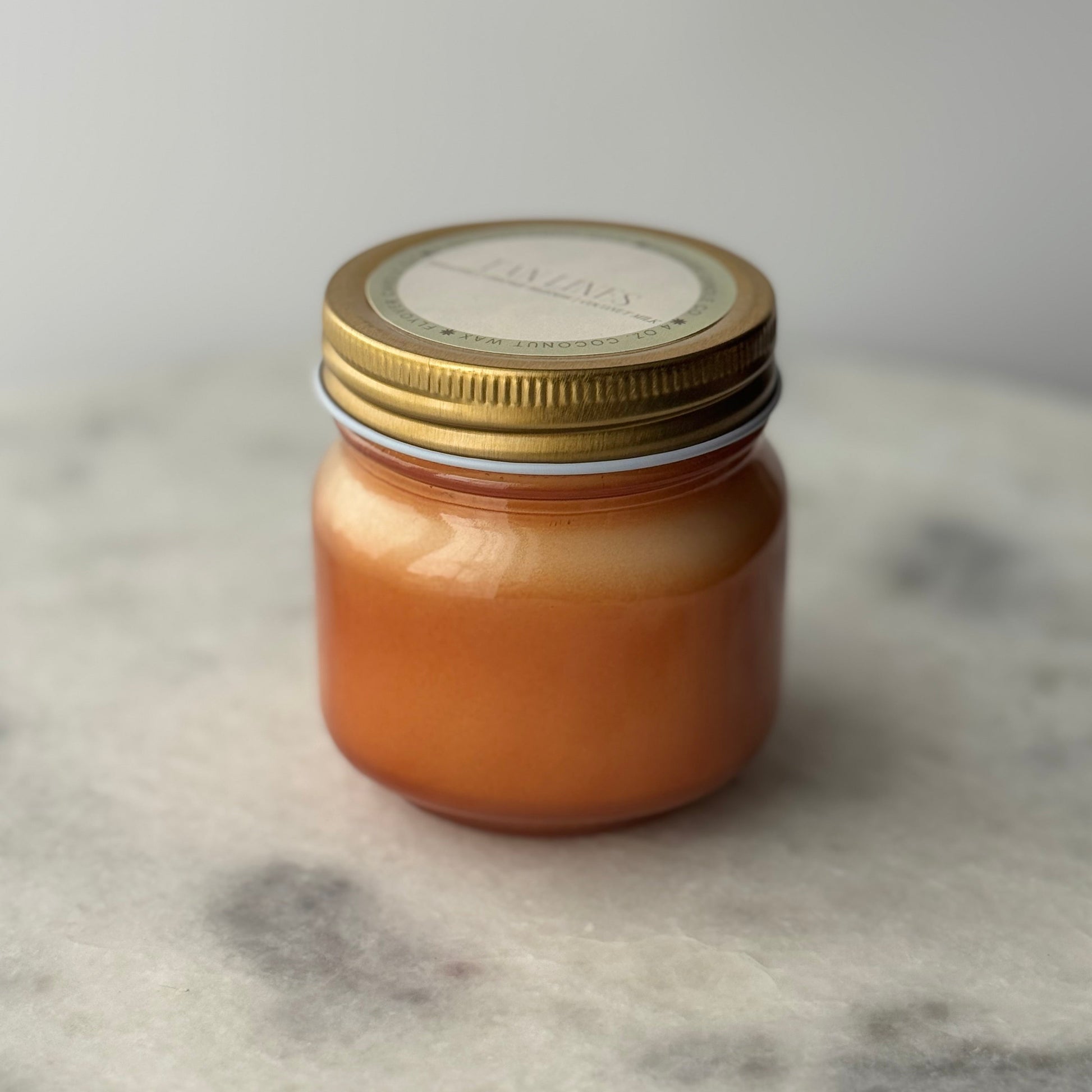 orange mason jar candle with a gold lid on a marble surface