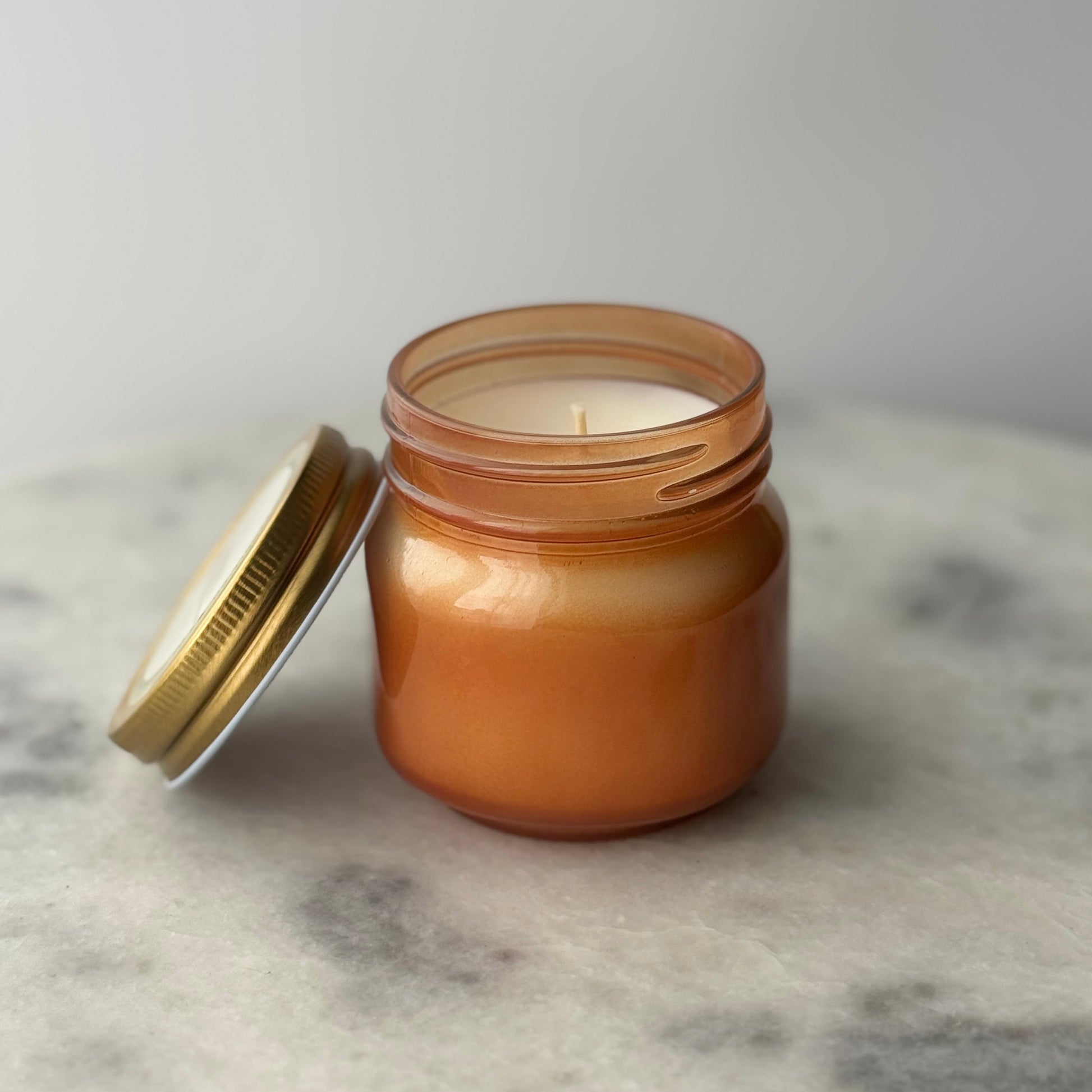 Candle in a glass jar with a metal lid on a marble surface