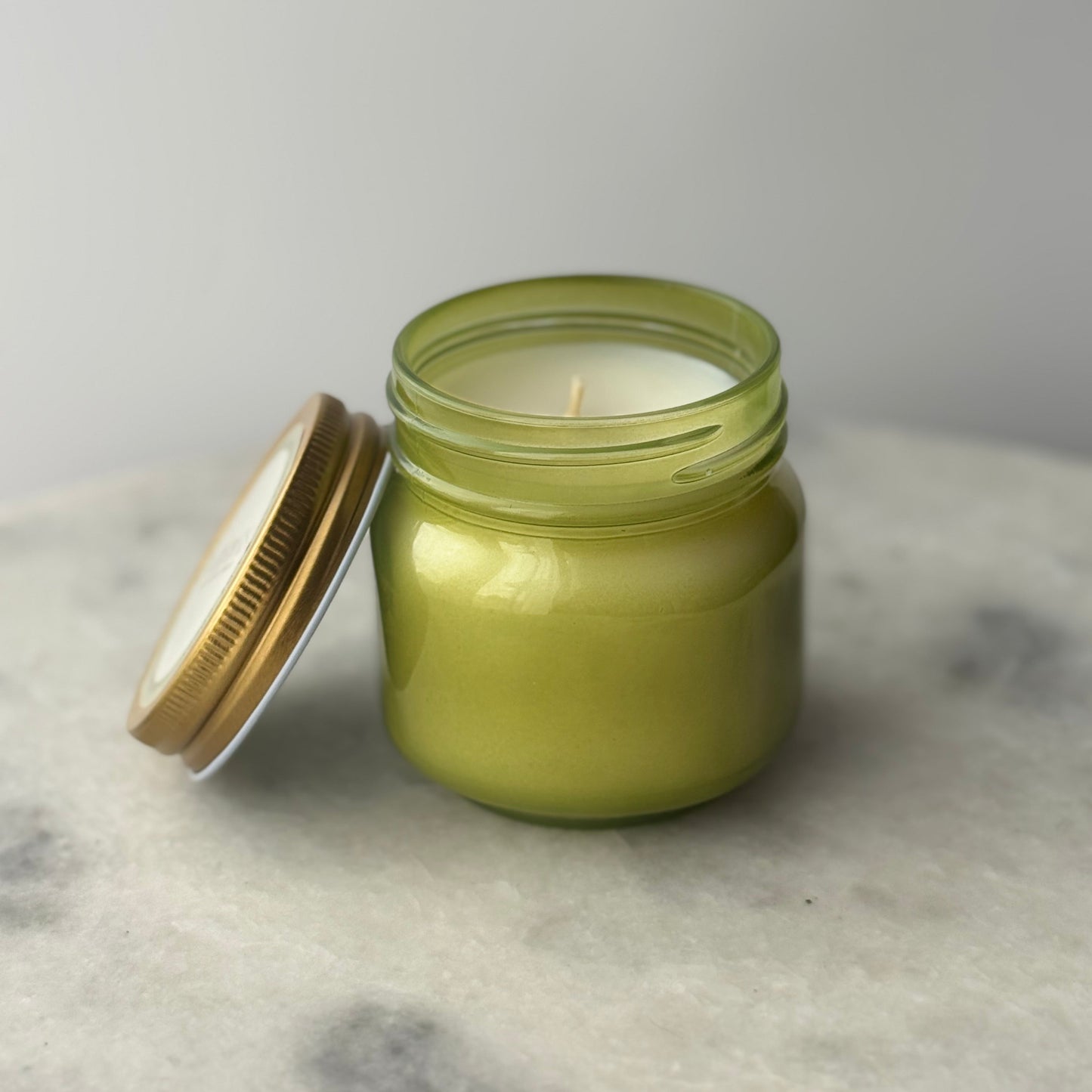 Green candle in a glass jar with a metal lid on a marble surface