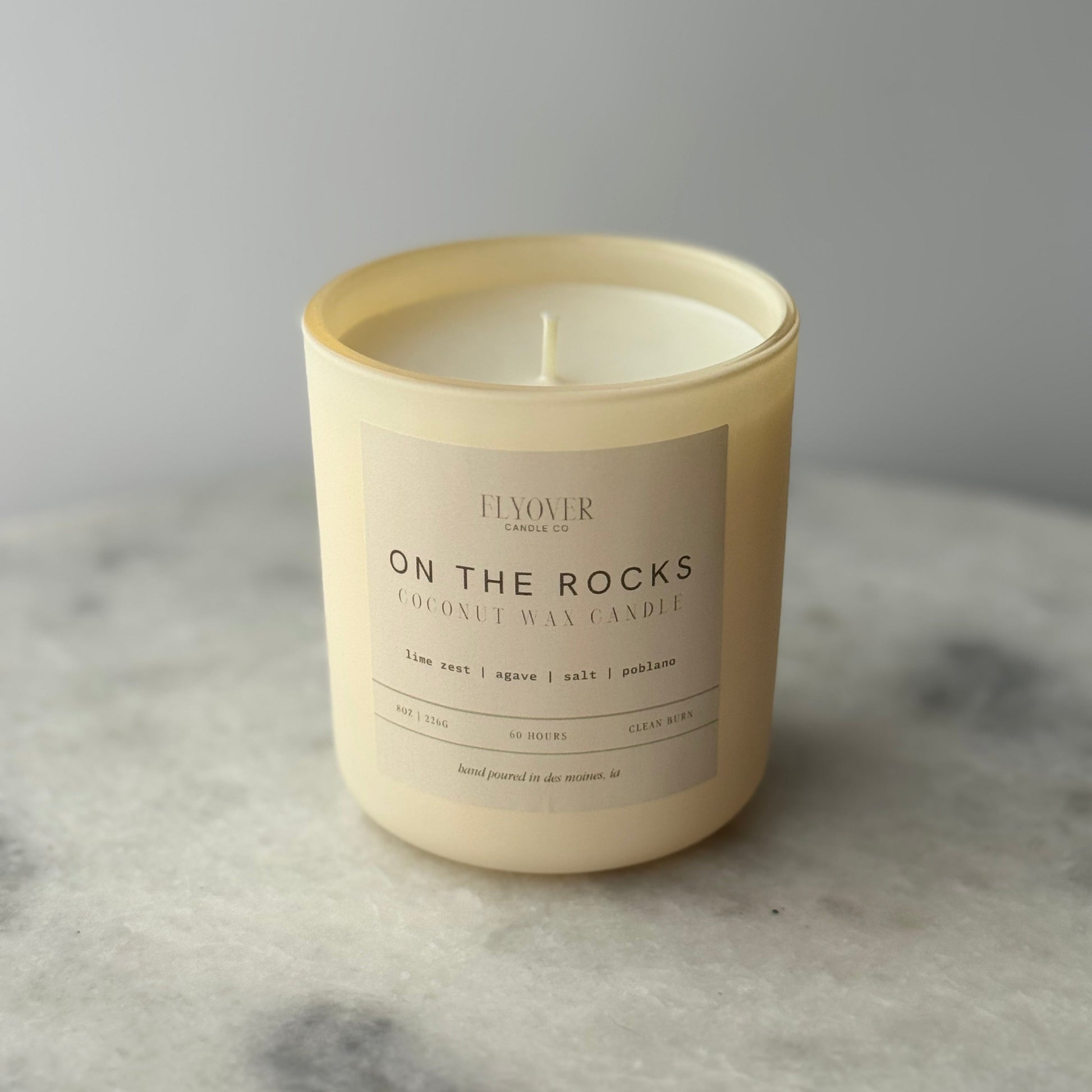 Candle labeled 'On the Rocks' by on a marble surface with a gray background